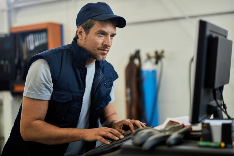 Car mechanic using computer while working in auto repair shop.